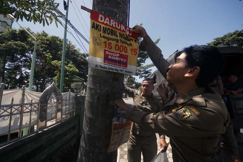 Petugas sempat beberapa kali kesulitan melepas banner dan spanduk lantaran menggunakan kawat dan paku. (Lampungnews /El Shinta)